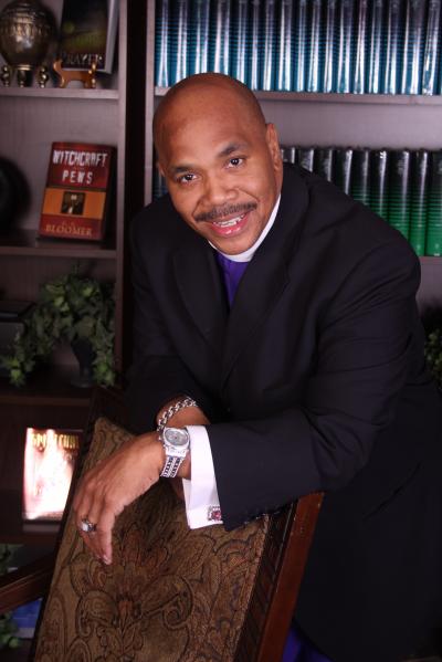 Smiling man in formal attire, leaning on chair.