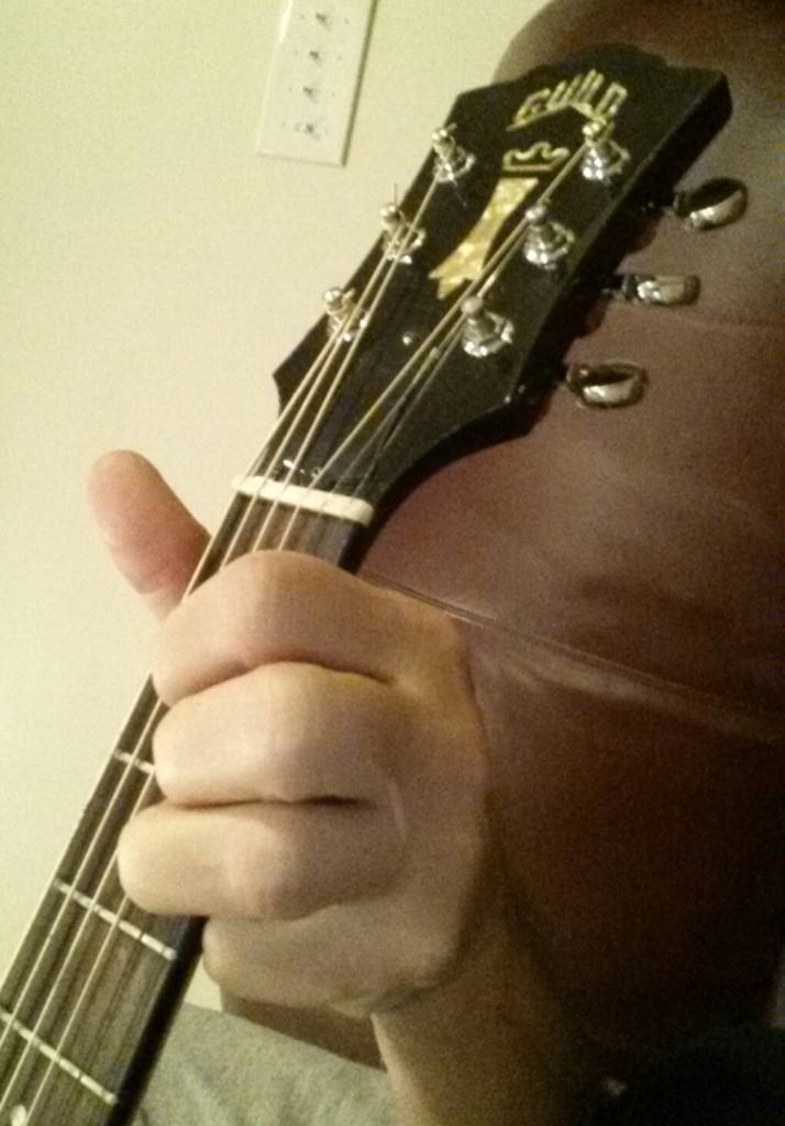 A person playing an acoustic guitar with one hand.