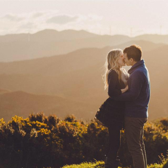 Couple kissing against a scenic mountain backdrop.