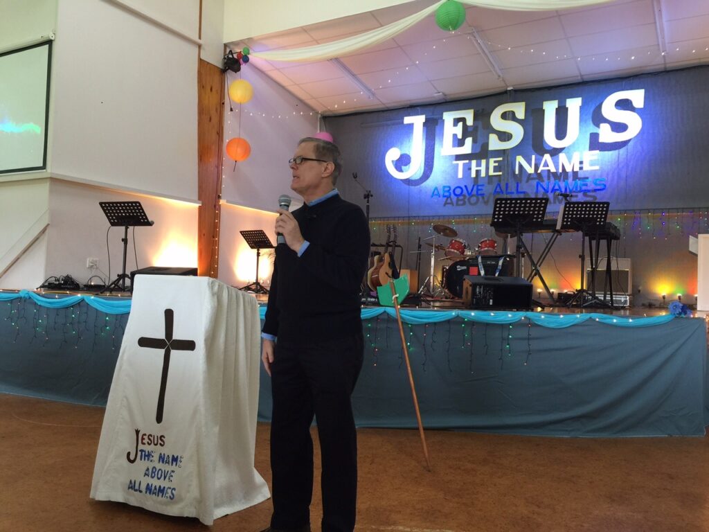 Speaker at church with "Jesus" backdrop.