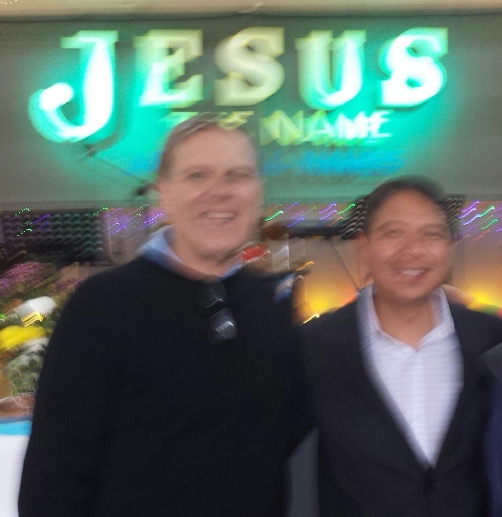 Two men standing in front of a jesus name sign.