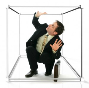 Man in a suit crouching inside a cube.