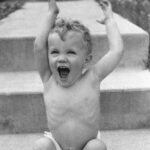 Happy child sitting on steps, arms raised.