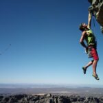 Climber hanging from a rock under clear sky.