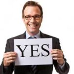 Smiling man holding "YES" sign.