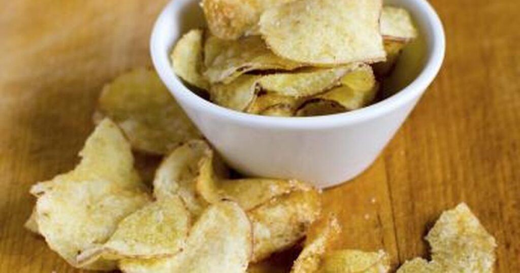 Bowl of potato chips on wooden surface.