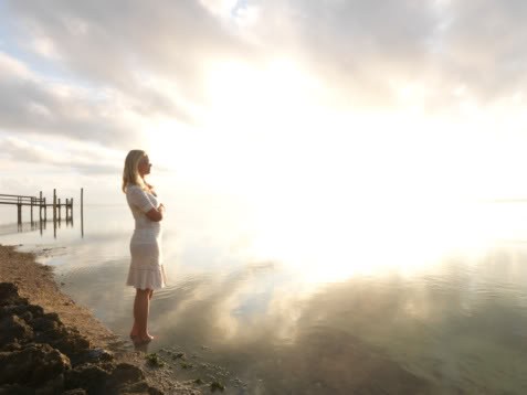 Woman standing by water at sunrise.