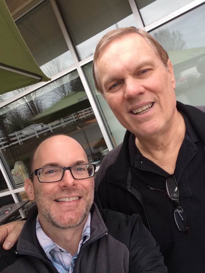 Two men smiling in a selfie outdoors.