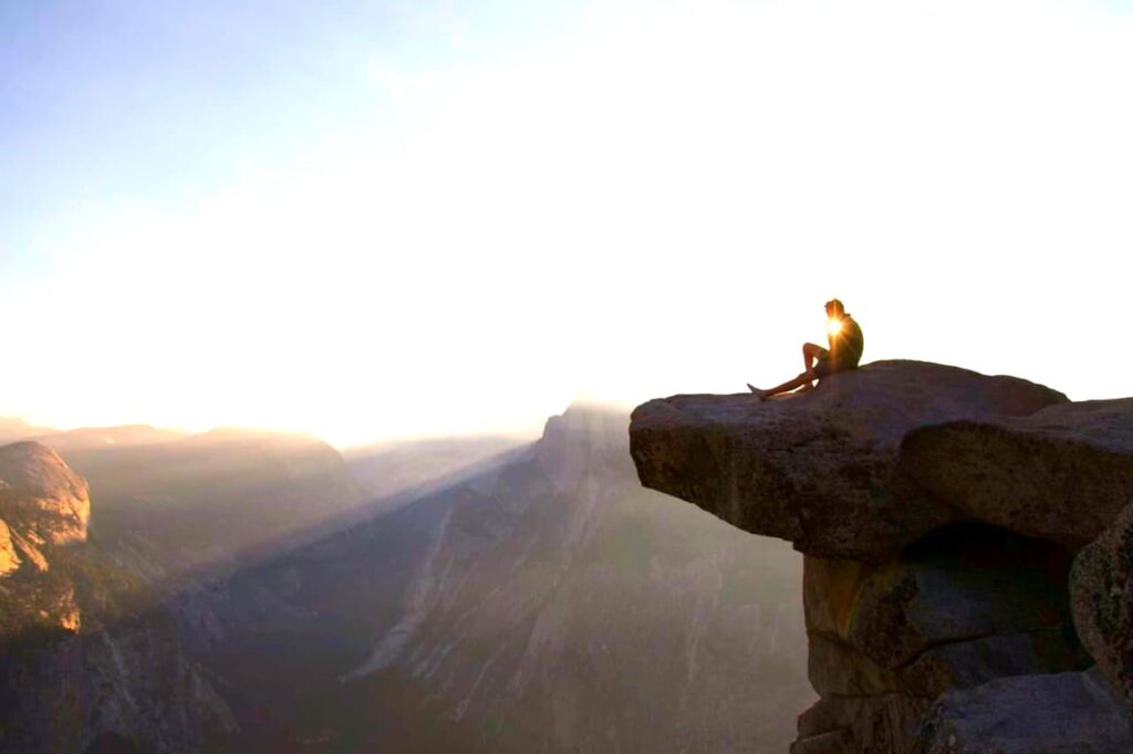 Person sitting on rock ledge at sunset.