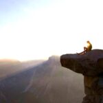 Person sitting on rock ledge at sunset.