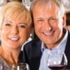 A man and woman smile while holding wine glasses.