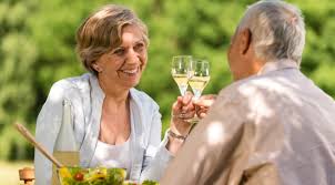 Elderly couple toasting with drinks outdoors.