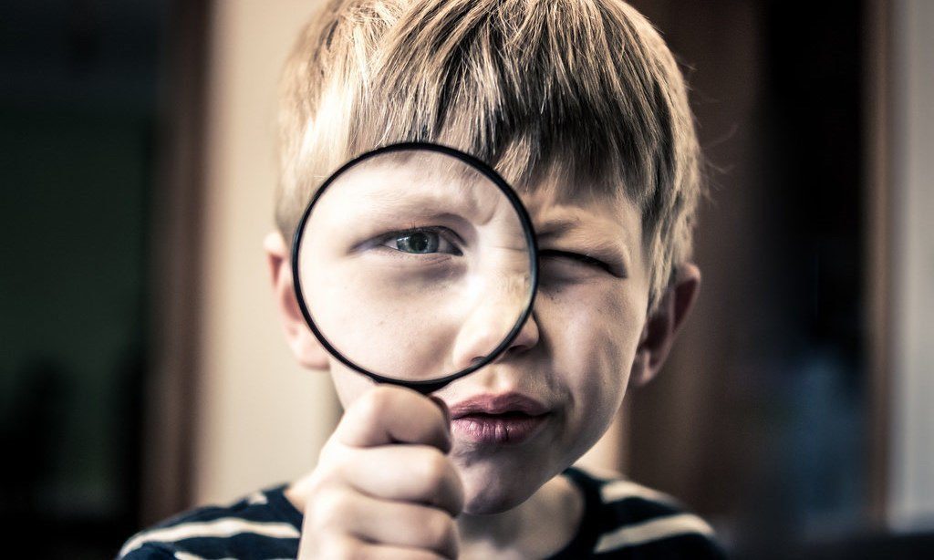 A boy holding up a magnifying glass to his eye.