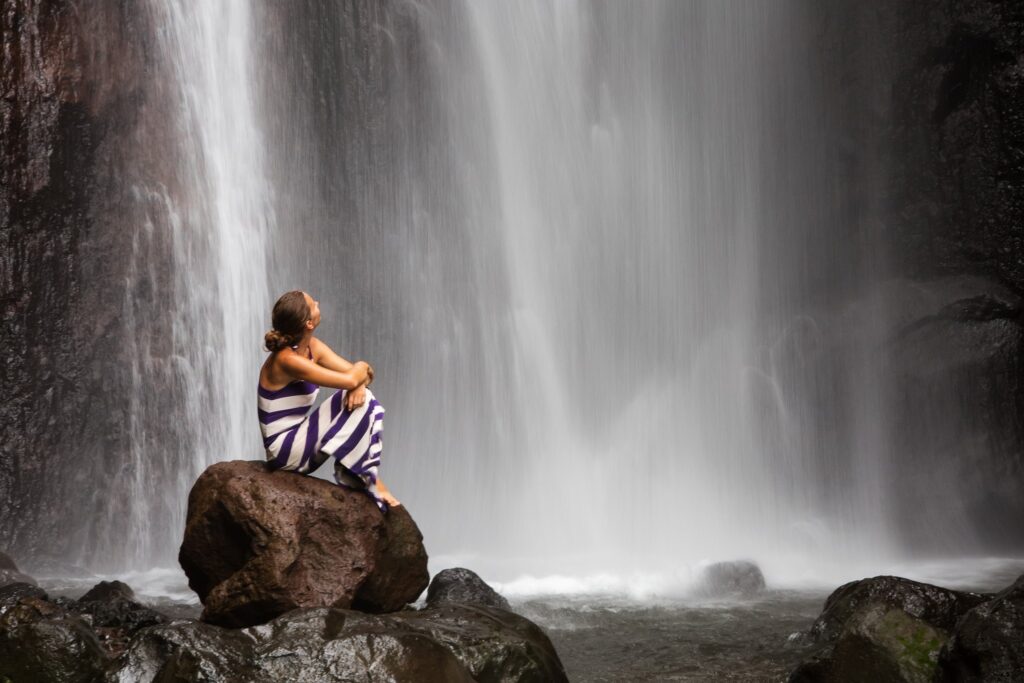 Woman sitting on rock by waterfall.