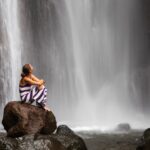 Woman sitting on rock by waterfall.