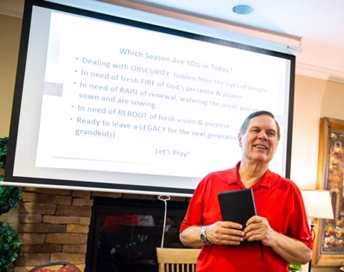 A man in red shirt holding a book while standing next to a projector screen.