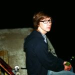 Young person with glasses sitting by skateboards.