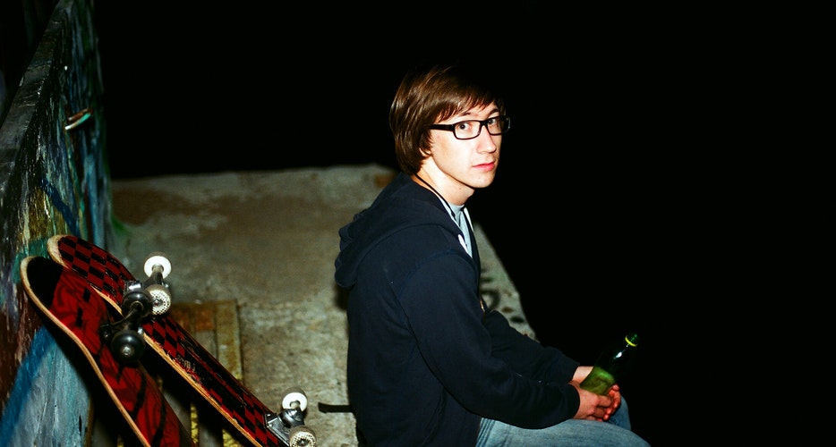 Young person with glasses sitting by skateboards.