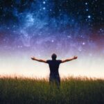 Person standing in grass under starry sky.