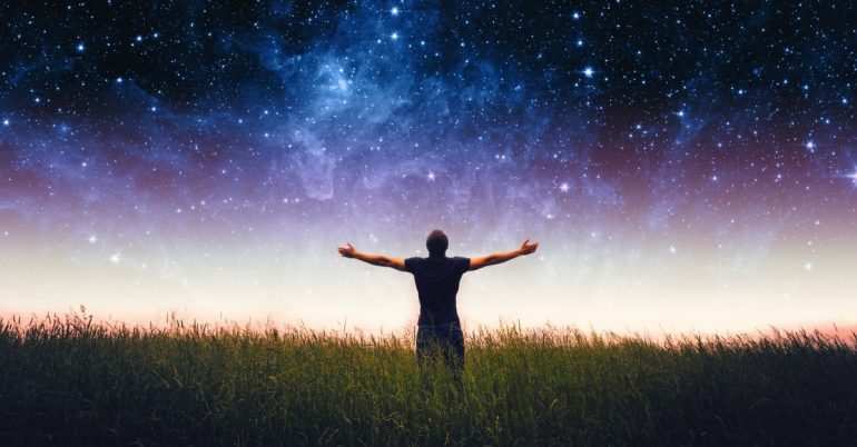 Person standing in grass under starry sky.