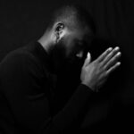 Person in prayer pose against dark background.