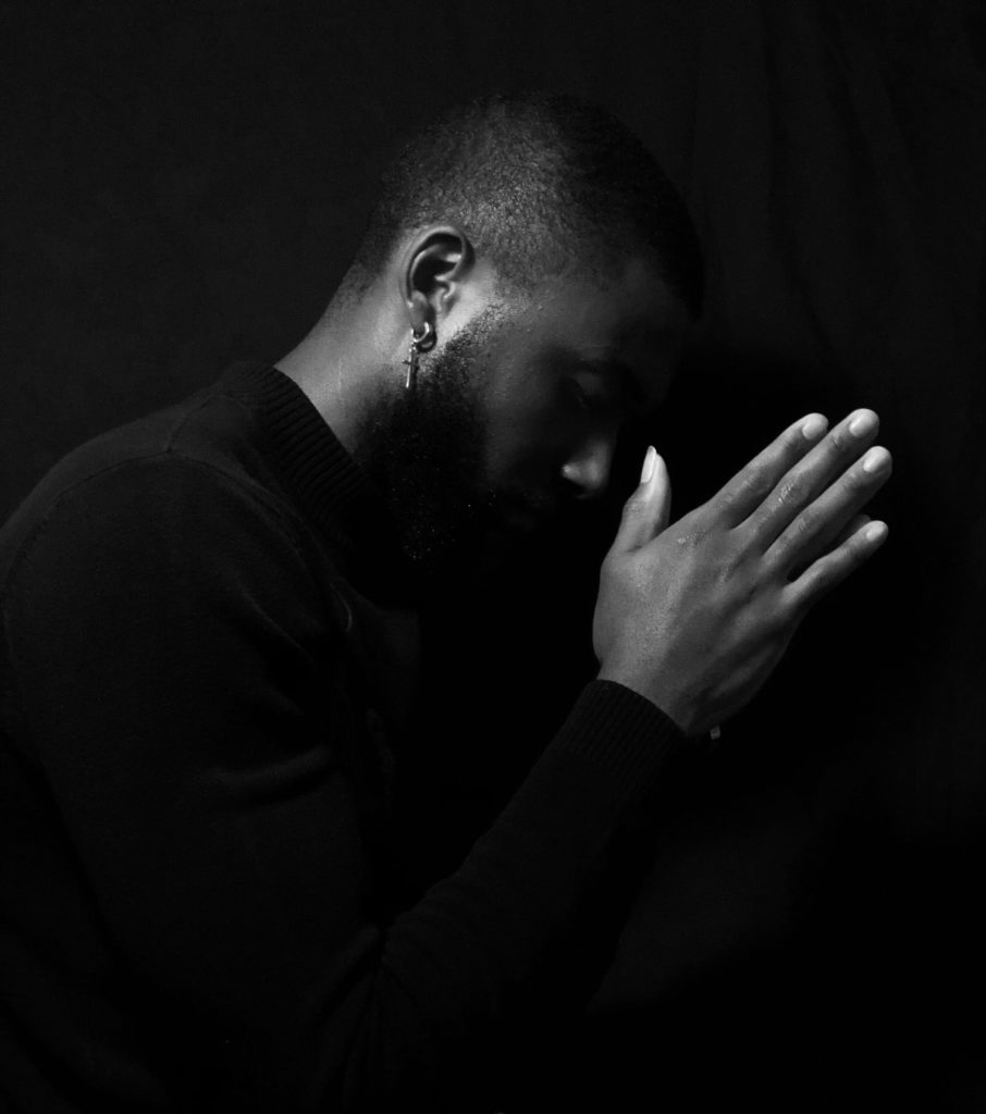 Person in prayer pose against dark background.