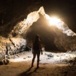 Person standing in a cave with sunlight.