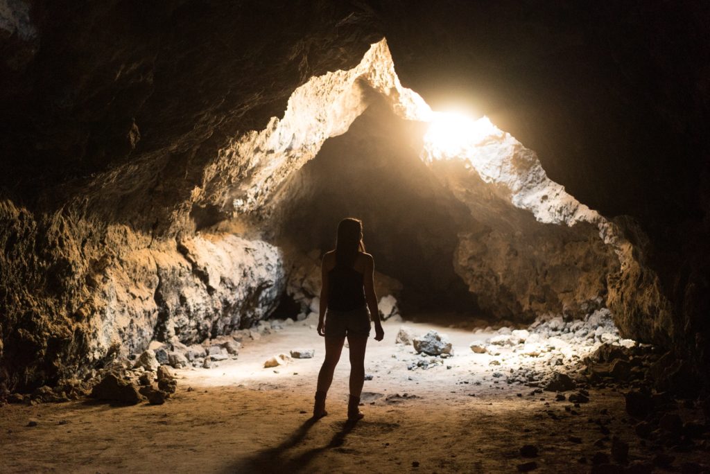 Person standing in a cave with sunlight.