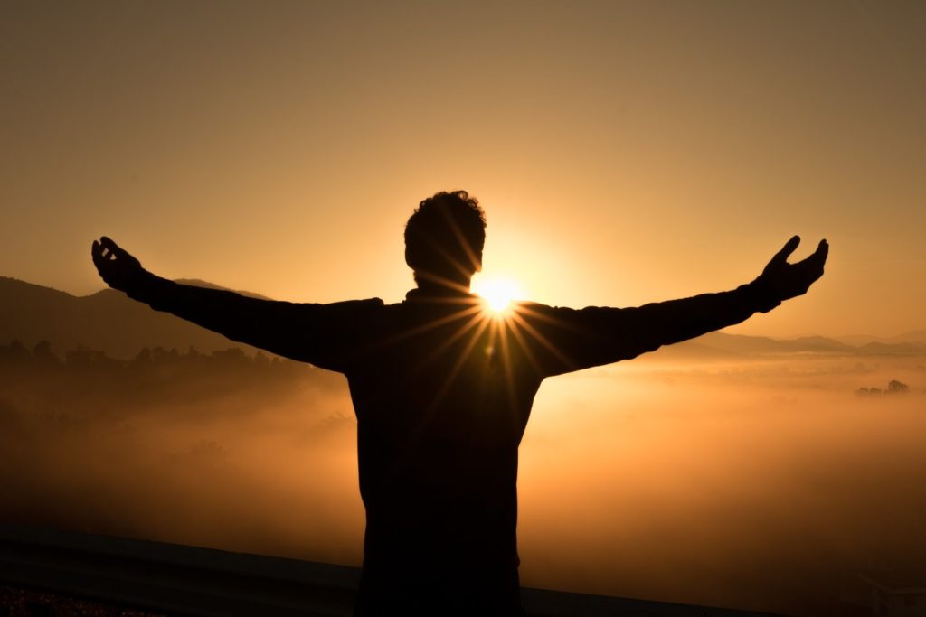 Silhouette of person embracing sunrise.