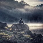 Person sitting on a rock by a lake.