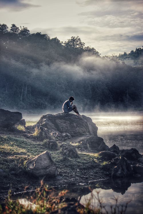 Person sitting on a rock by a lake.