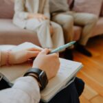 Person writing in notebook, two people nearby.