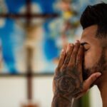 Man with tattoos praying in a serene setting.