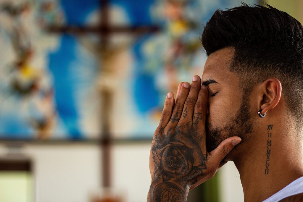 Man with tattoos praying in a serene setting.