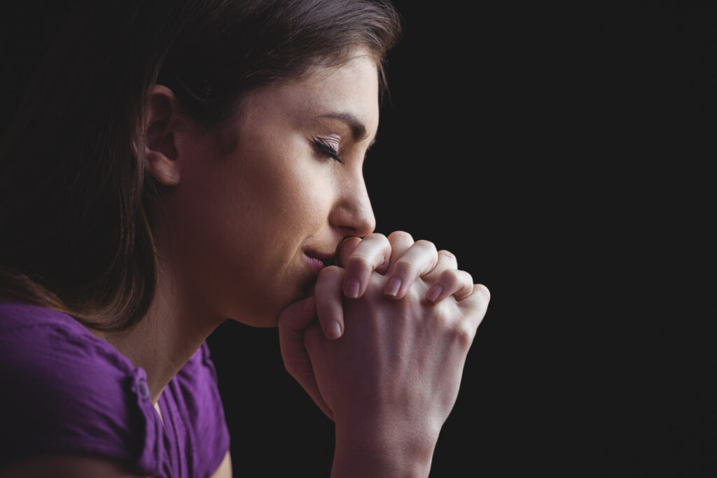 Woman in contemplation, hands clasped together.