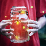 Child holding a jar of glowing fireflies.