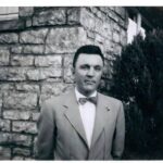 Man in suit standing by stone wall.