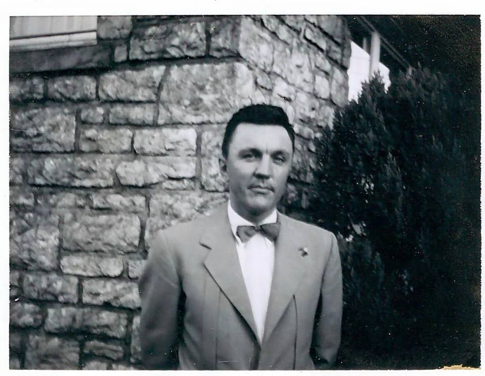 Man in suit standing by stone wall.