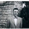 A man in a suit and bow tie standing next to a brick wall.