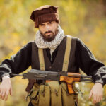 Bearded man with rifle in autumn setting.